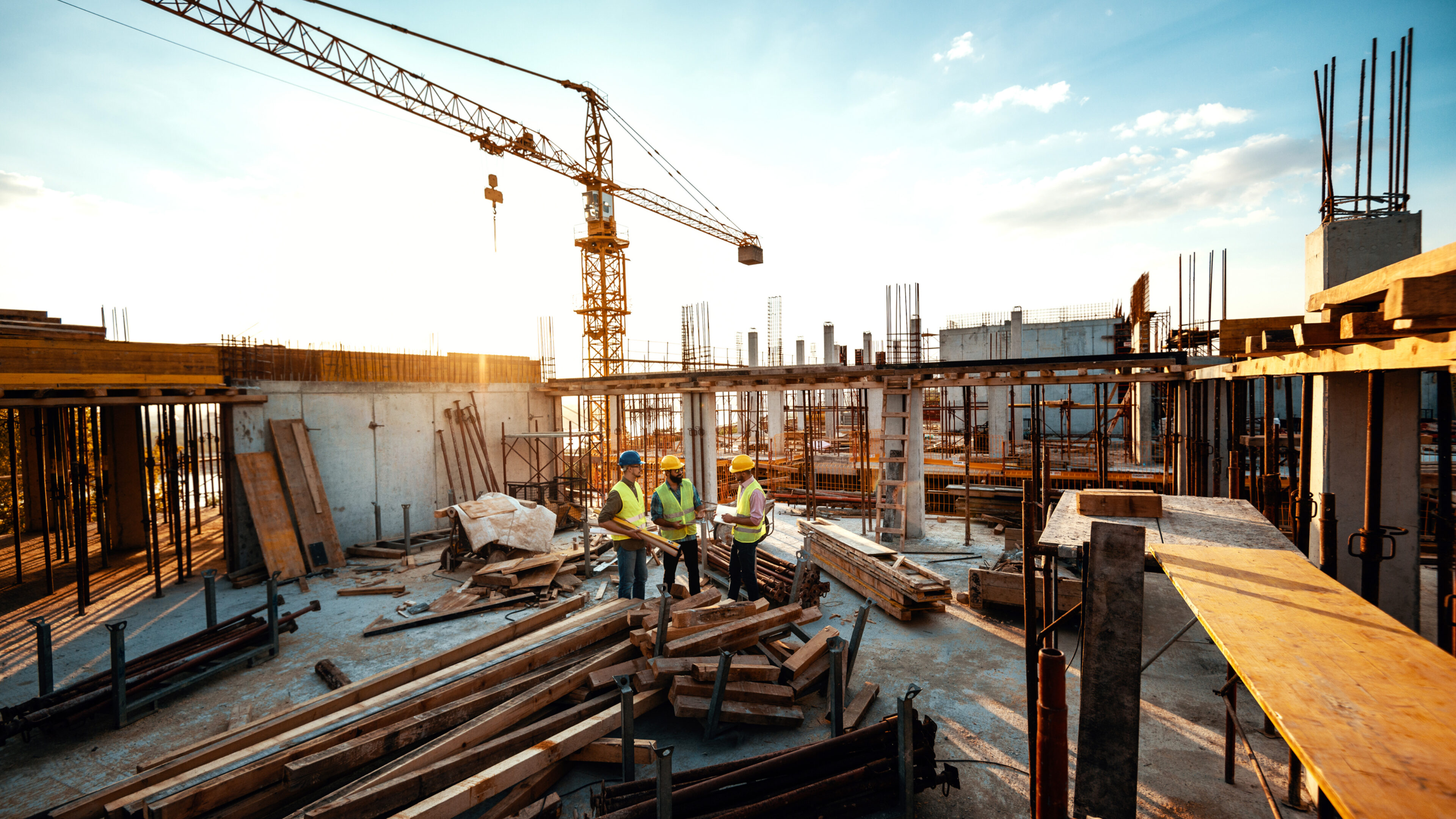 Aufnahme von einer großen Baustelle Menschen in Sicherheitskleidung, mit Baumaterial und einem Kran im Hintergrund