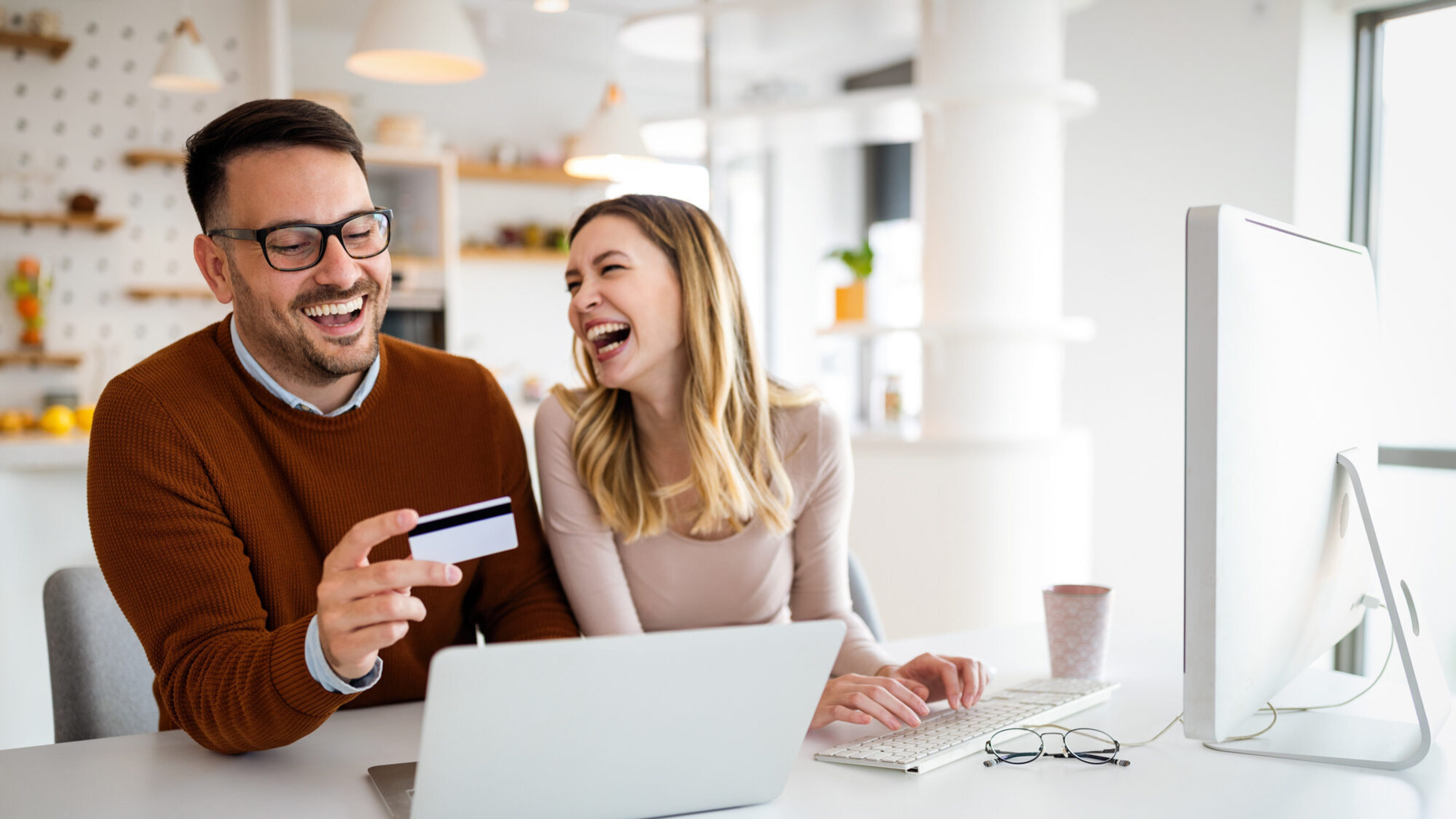 Portrait von einem Pärchen, dass freudig vor dem Laptop im Büro online shopping betreibt