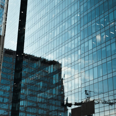Nahaufnahme eines Wolkenkratzer mit Glasfassade und einer Reflektion von weiteren modernen Gebäuden