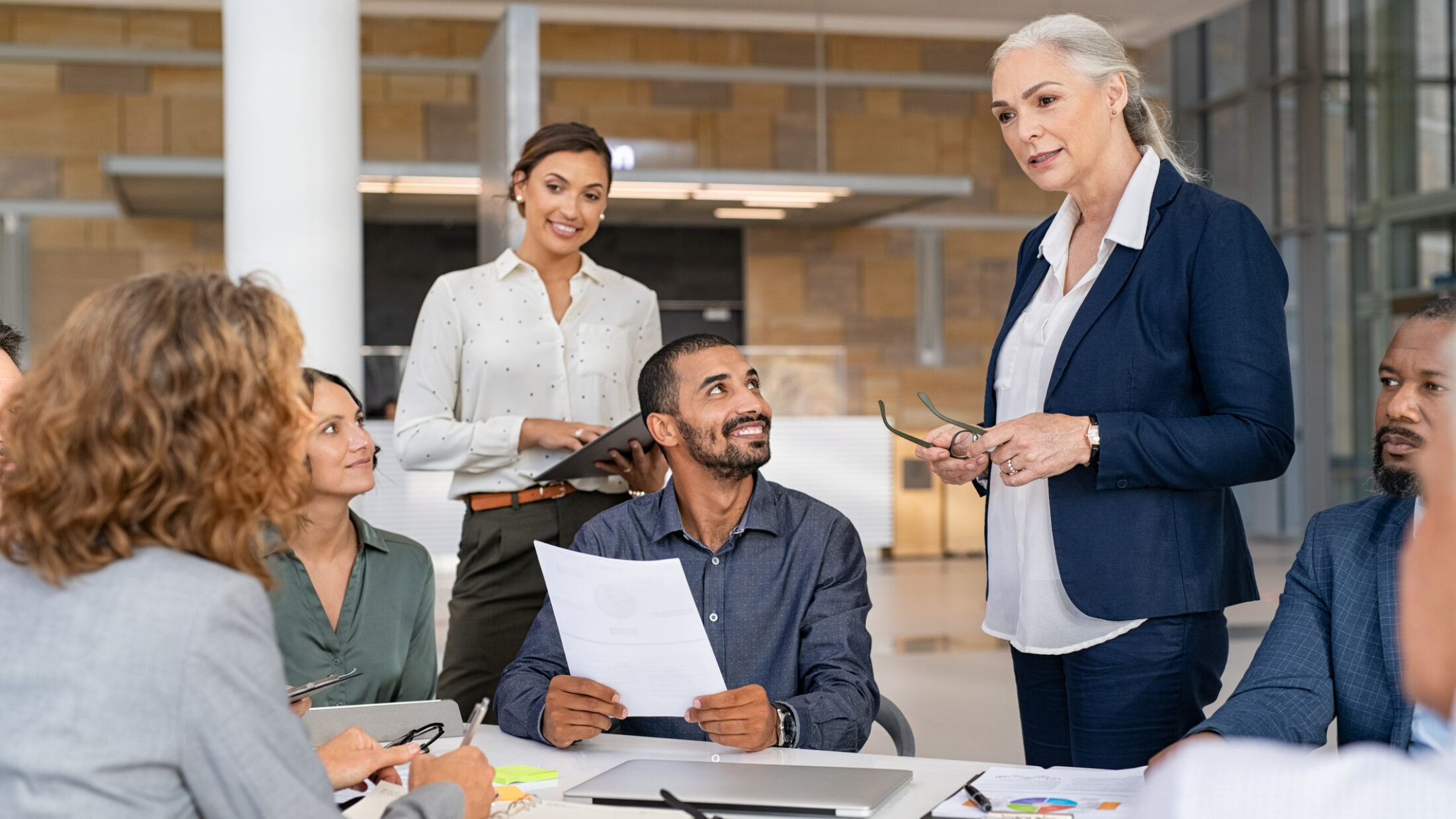 Eine Gruppe von Personen sitzt in einem Stuhlkreis, während eine stehende Person die Runde anleitet und ein Führungsgespräch oder Team-Meeting moderiert.