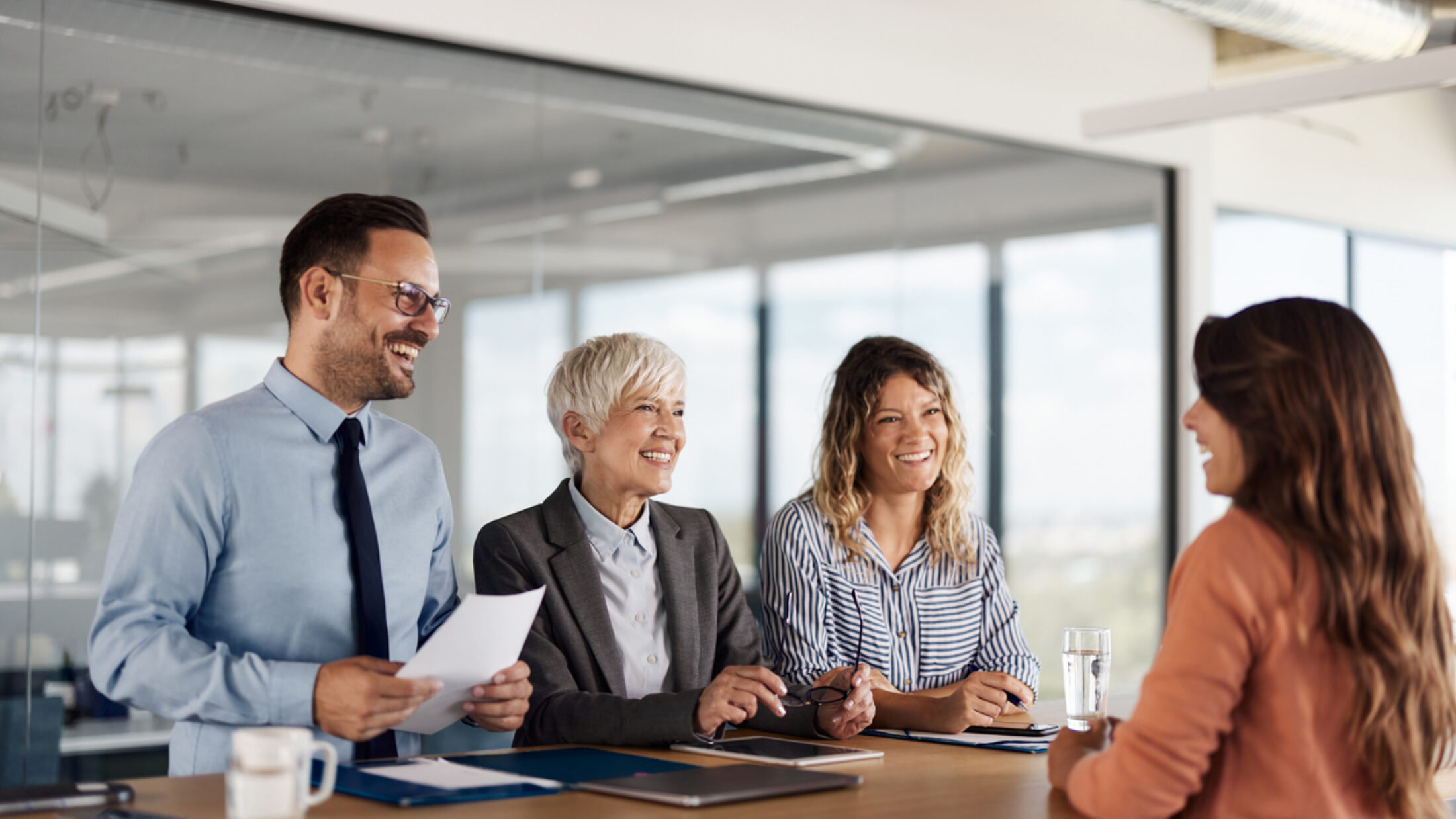 Vier Personen sitzen in einem modernen Konferenzraum an einem Tisch und führen ein Bewerbungsgespräch mit einer weiteren Person, die ihnen gegenübersitzt.