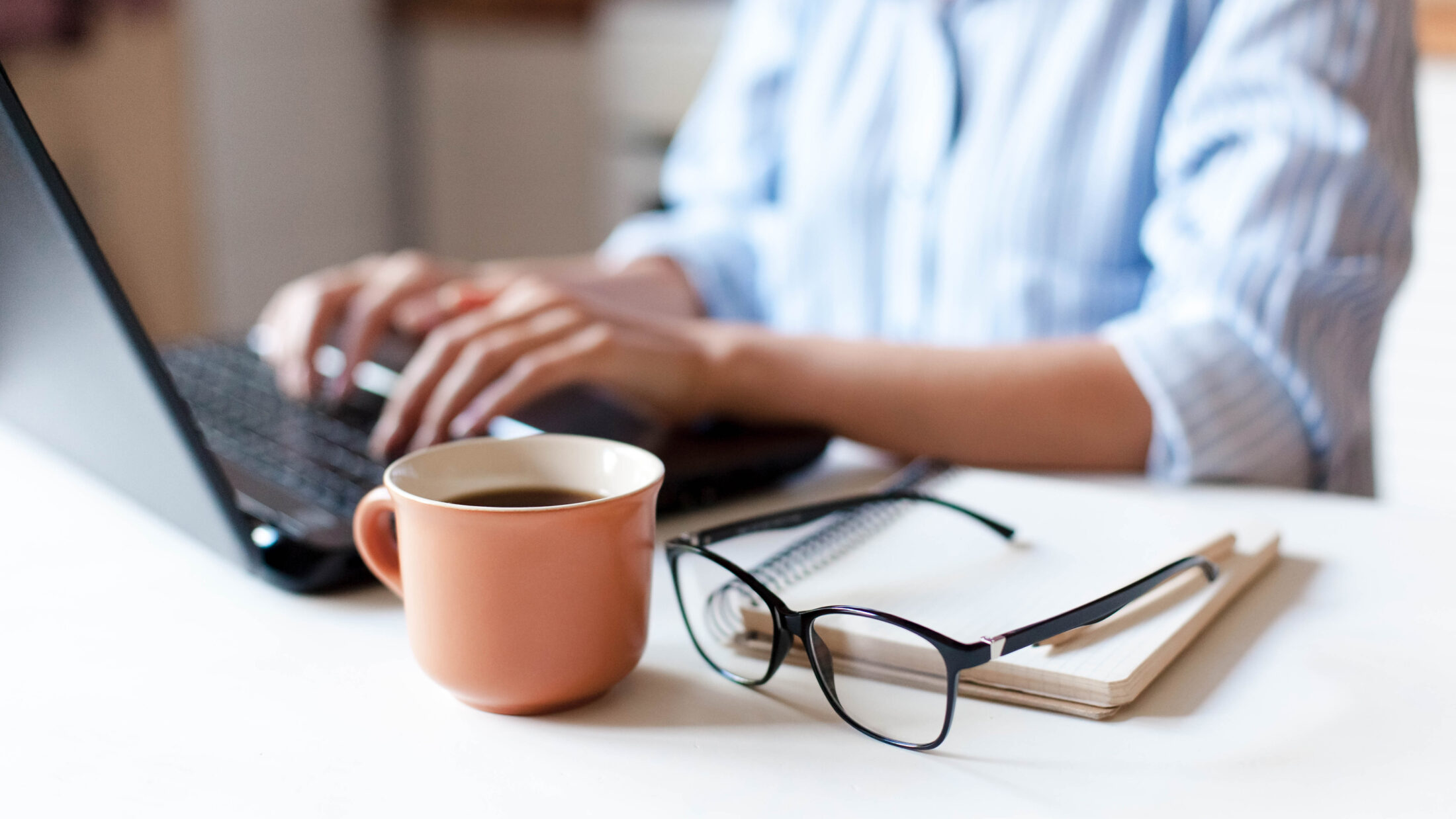 Frau vom Remote-Arbeitsplatz in der Küche mit Laptop, Tasse Kaffee, Brille