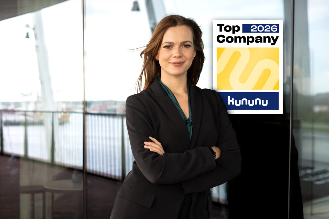 Eine Frau steht an ein Fenster gelehnt, über ihrer linken Schulter befindet sich eine Grafik mit der Aufschrift "Top Company 2026"