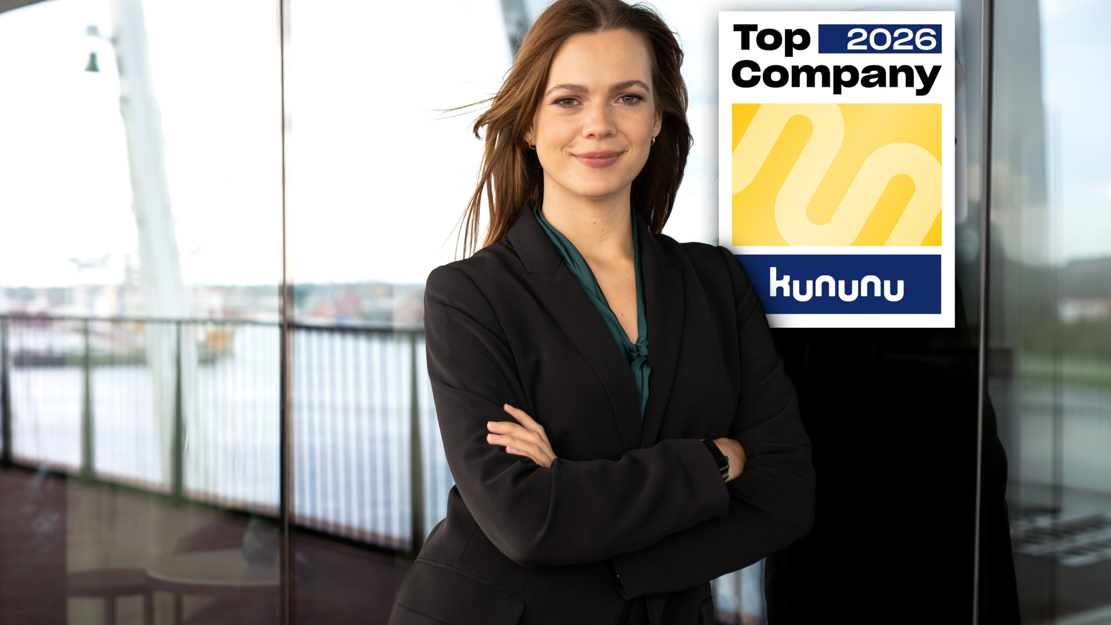 Eine Frau steht an ein Fenster gelehnt, über ihrer linken Schulter befindet sich eine Grafik mit der Aufschrift "Top Company 2026"